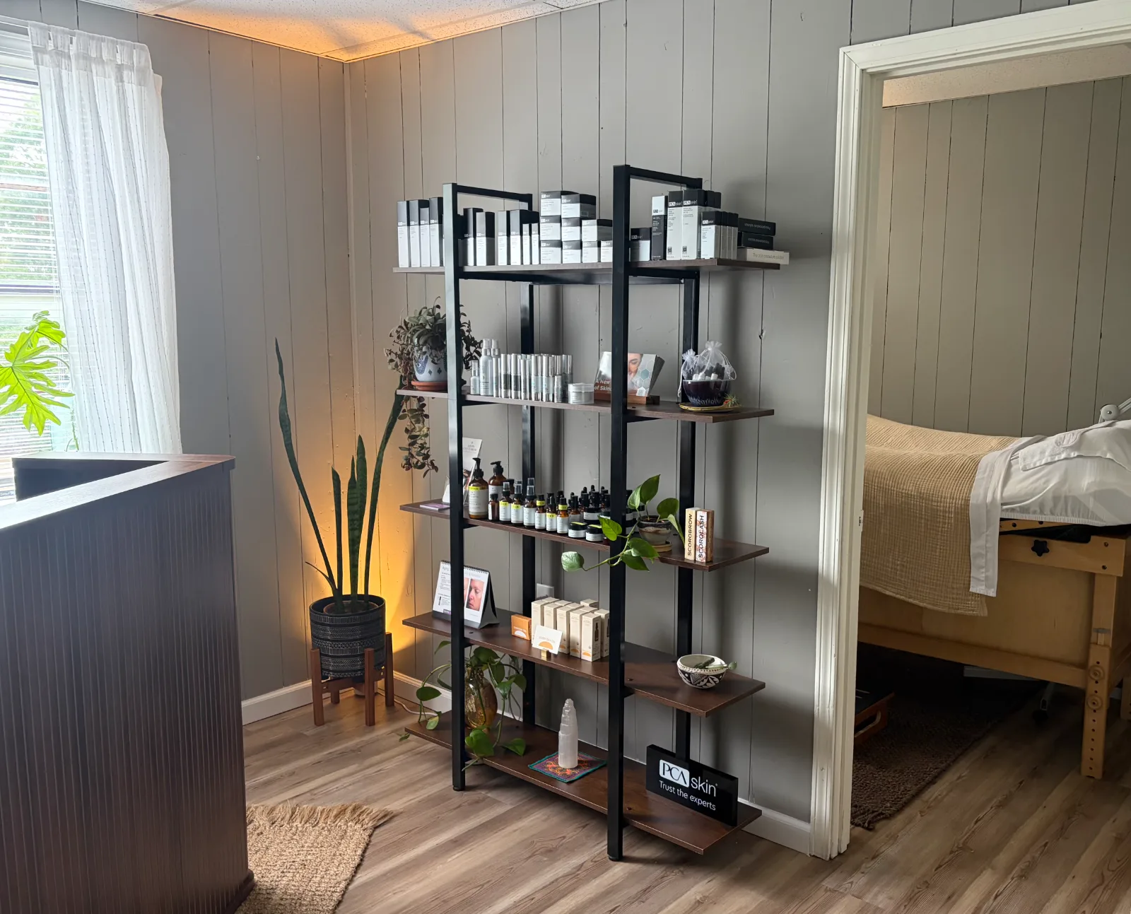 The studio's retail shelf with PCA SKIN and plant-based product lines among houseplants, with the treatment room beyond